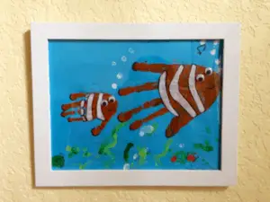 A painting showing adult and child handprints in orange paint with white stripes added to look like clownfish against a blue underwater background.