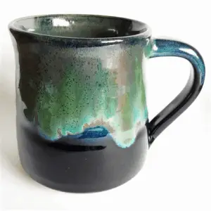 A ceramic mug glazed in black with a dripped glaze layer of green, white, and blue.
