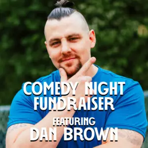 headshot of Dan Brown, a white man with dark hair worn in a ponytail and a dark goatee, wearing a bright blue t-shirt.